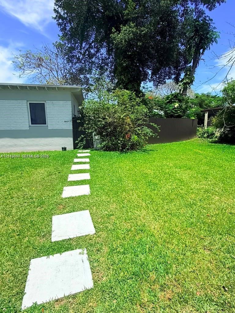 Expansive backyard featuring a manicured lawn, stone paver pathway, privacy fencing, and mature trees