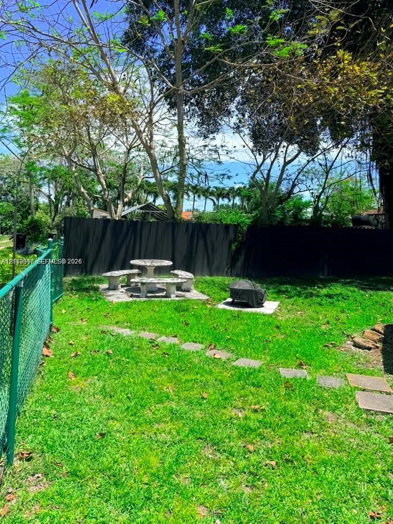 Private backyard featuring a chain-link perimeter fence, dark solid-panel privacy screening, stone paver stepping stones, and mature trees