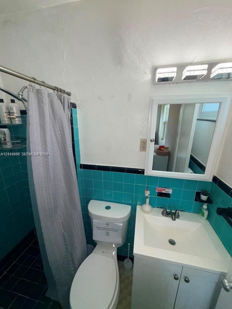 Bathroom featuring teal wall tiling with black accent trim, a white vanity with an integrated sink, a medicine cabinet, and a multi-bulb light fixture