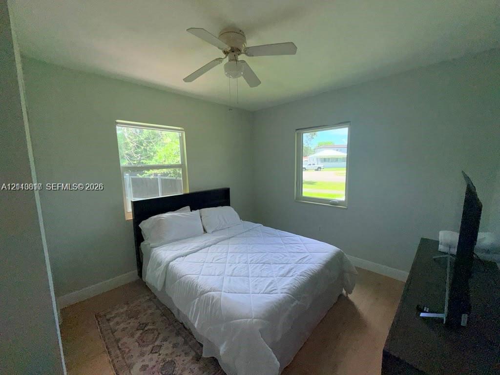 Bedroom featuring light-toned wood-finish flooring, two large windows, and a central ceiling fan with integrated lighting