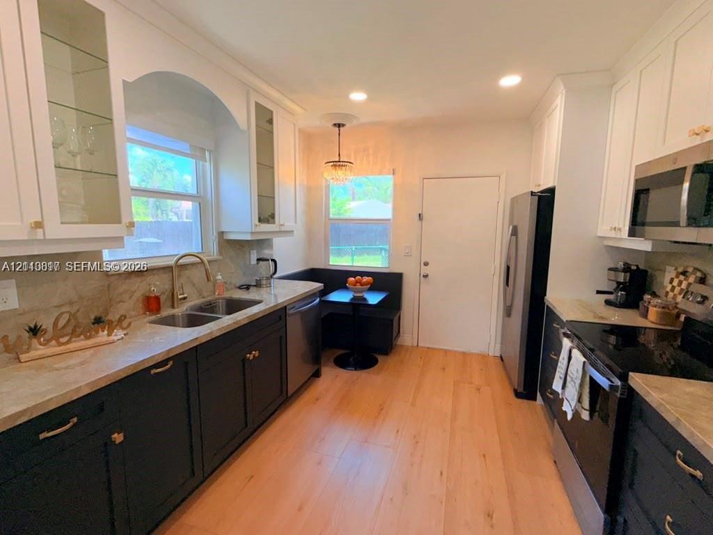 Kitchen featuring white upper cabinetry, dark base cabinetry, wood-finish flooring, stone-surfaced countertops, and stainless steel appliances