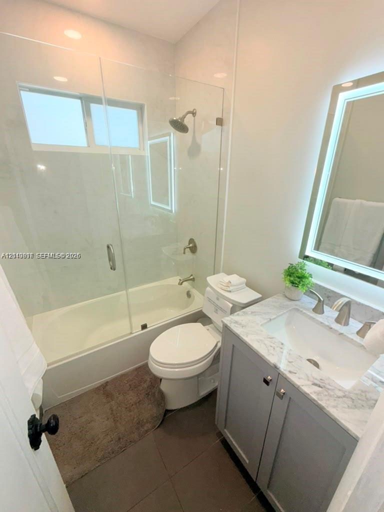Bathroom featuring a vanity with a stone-top counter, undermount sink, and integrated LED-lit mirror, paired with a glass-enclosed shower and tub combination featuring stone-finish wall tile