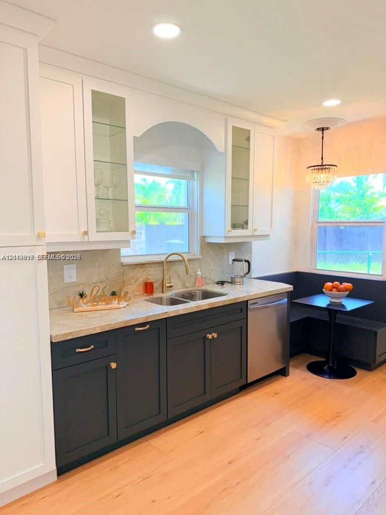 Two-toned cabinetry with glass-front display uppers, light-toned stone countertops, integrated stainless steel dishwasher, brass-finish faucet, and recessed lighting
