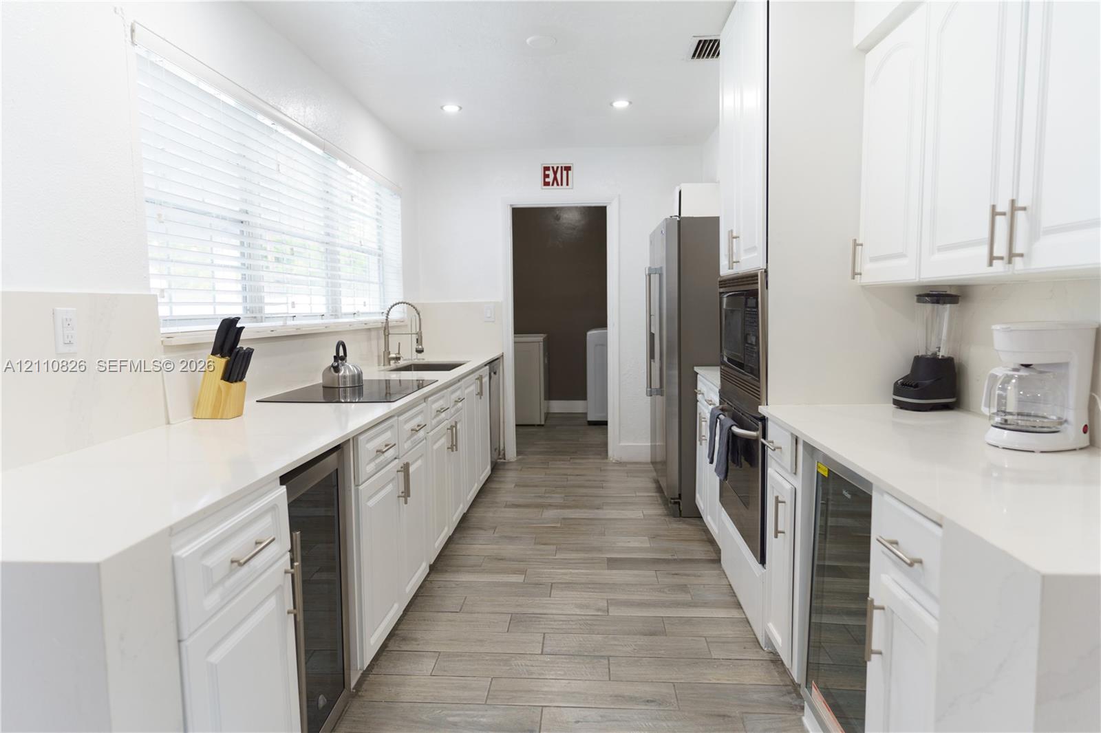 Kitchen featuring white cabinetry, solid-surface countertops, wood-finish tile flooring, a built-in double oven, and stainless steel integrated wine refrigerators