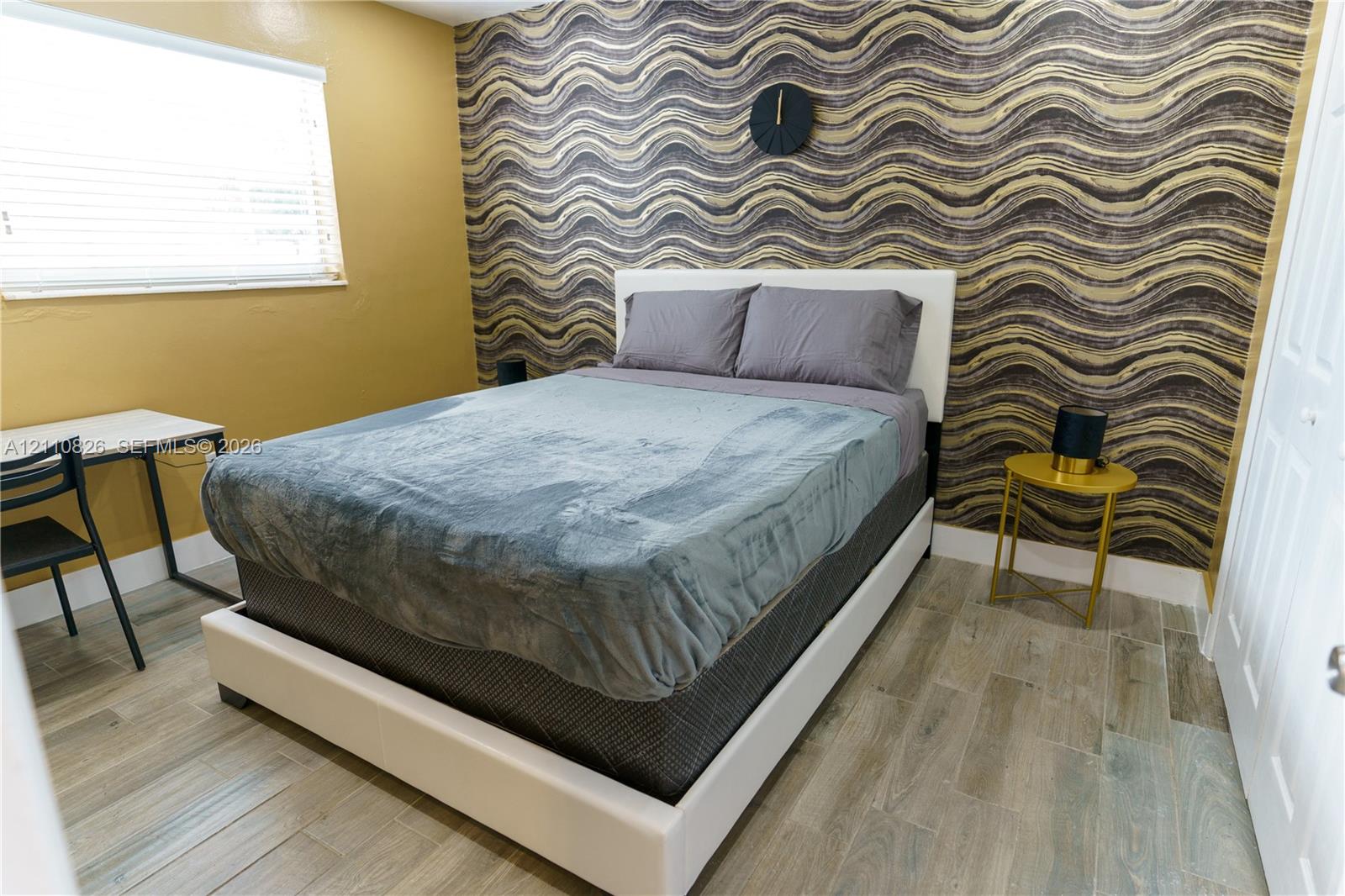 Room featuring patterned accent wall, wood-finish flooring, and horizontal blind window treatment