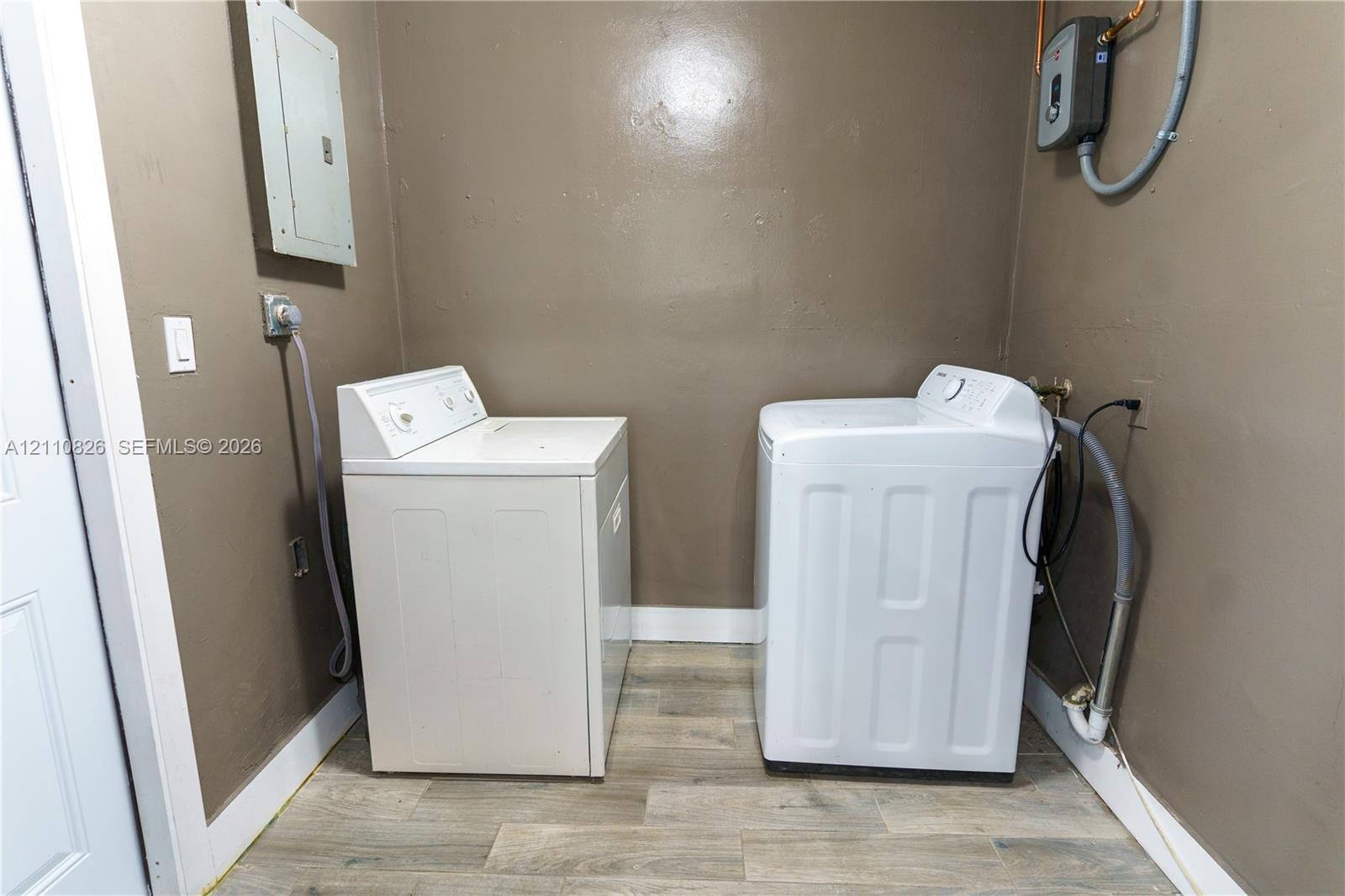 Dedicated laundry space featuring wood-finish flooring, integrated electrical panel, and wall-mounted water heater