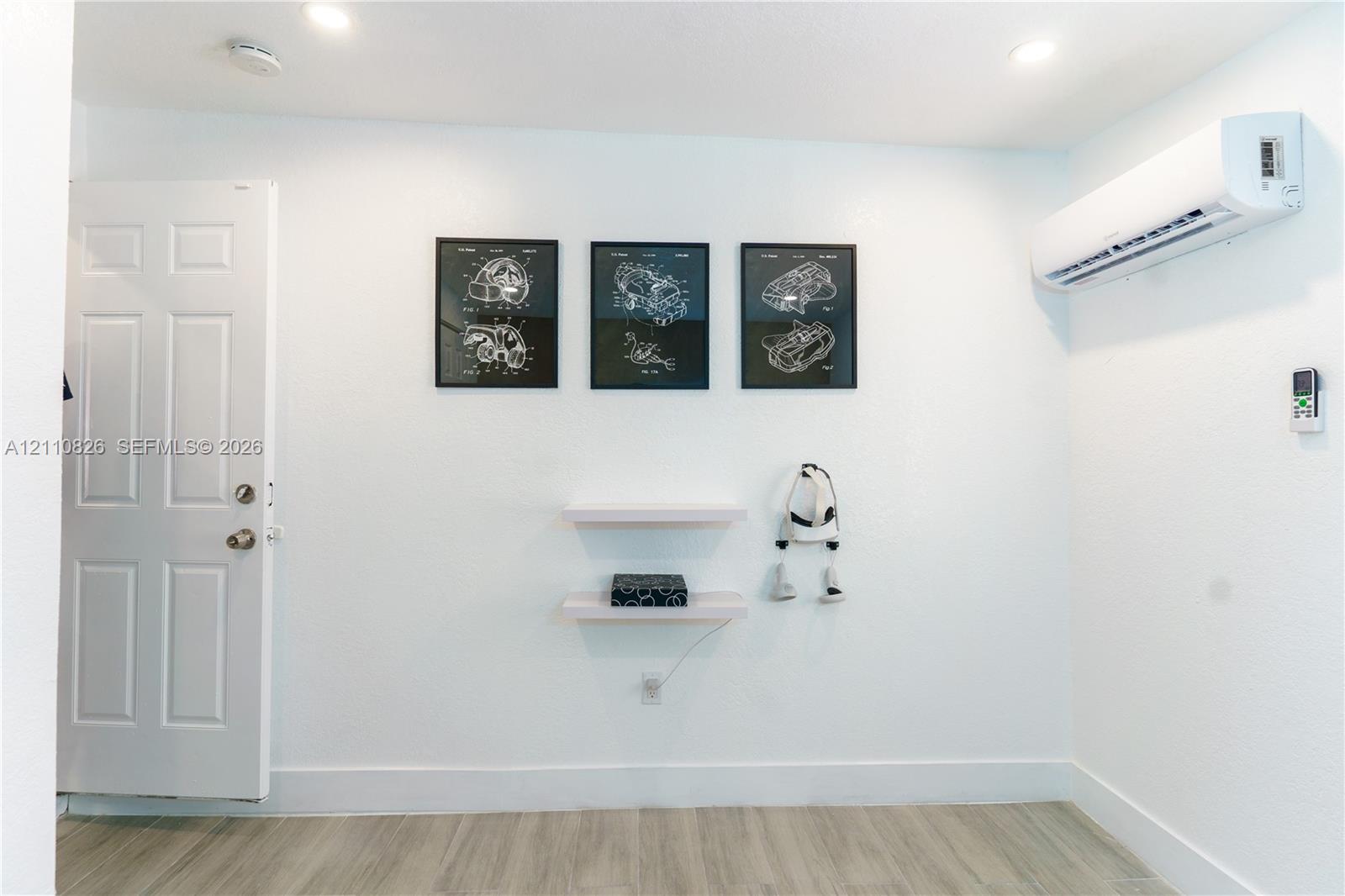 Interior space featuring wood-finish flooring, a wall-mounted ductless mini-split air conditioning unit, recessed ceiling lighting, and two minimalist floating shelves