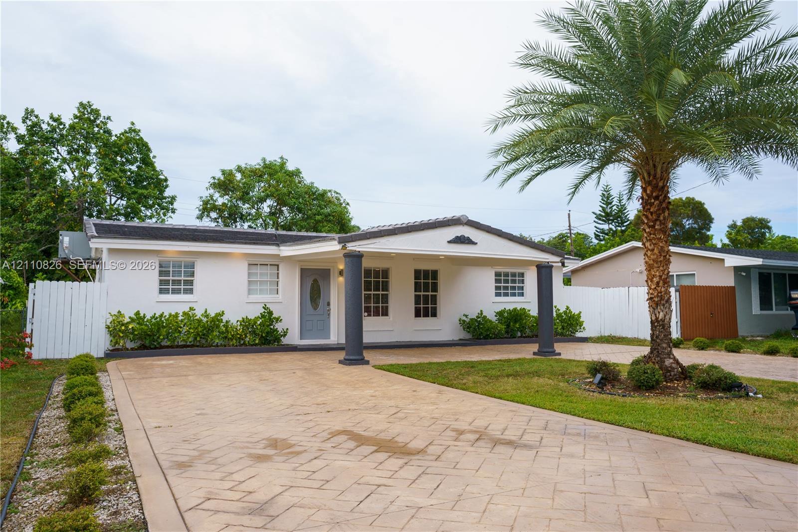 Single-story exterior featuring a paved herringbone driveway, a covered entryway with structural columns, and low-maintenance landscaping