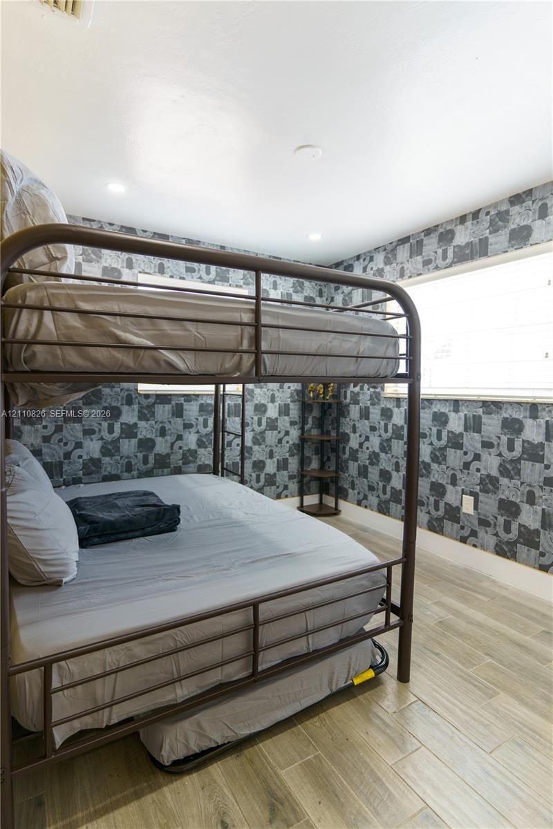 Room featuring wood-finish flooring, patterned wallpaper, and horizontal blinds