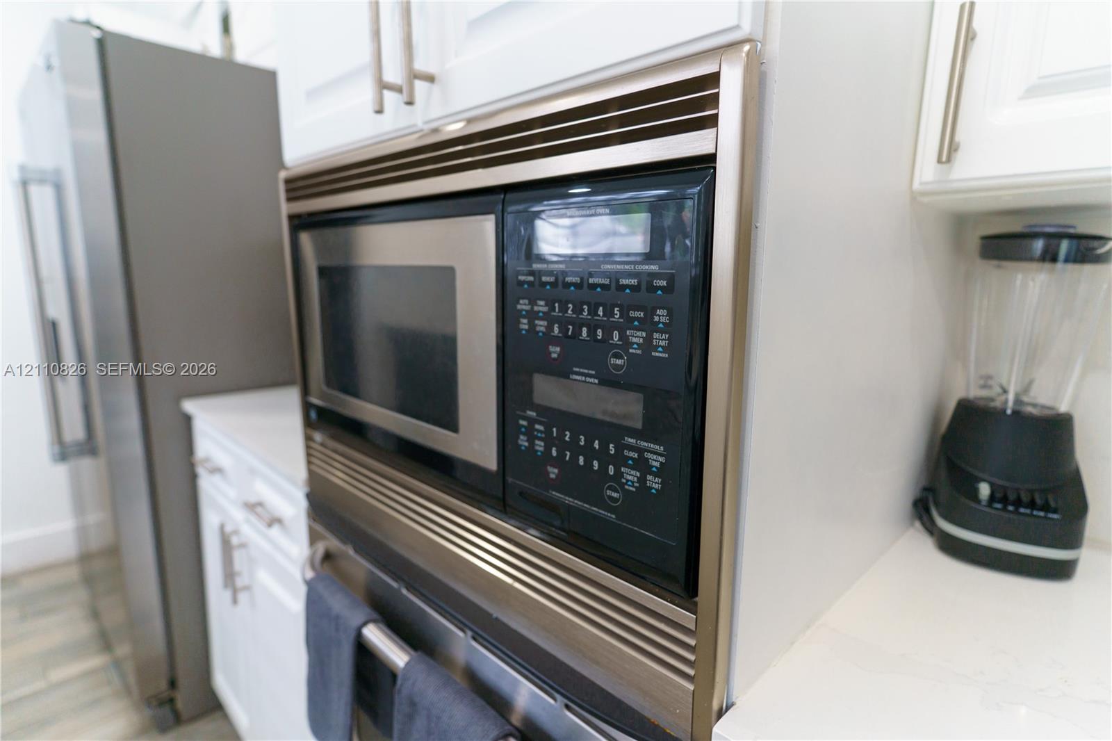 Built-in stainless steel microwave oven, white cabinetry featuring brushed metal hardware, and solid-surface countertops