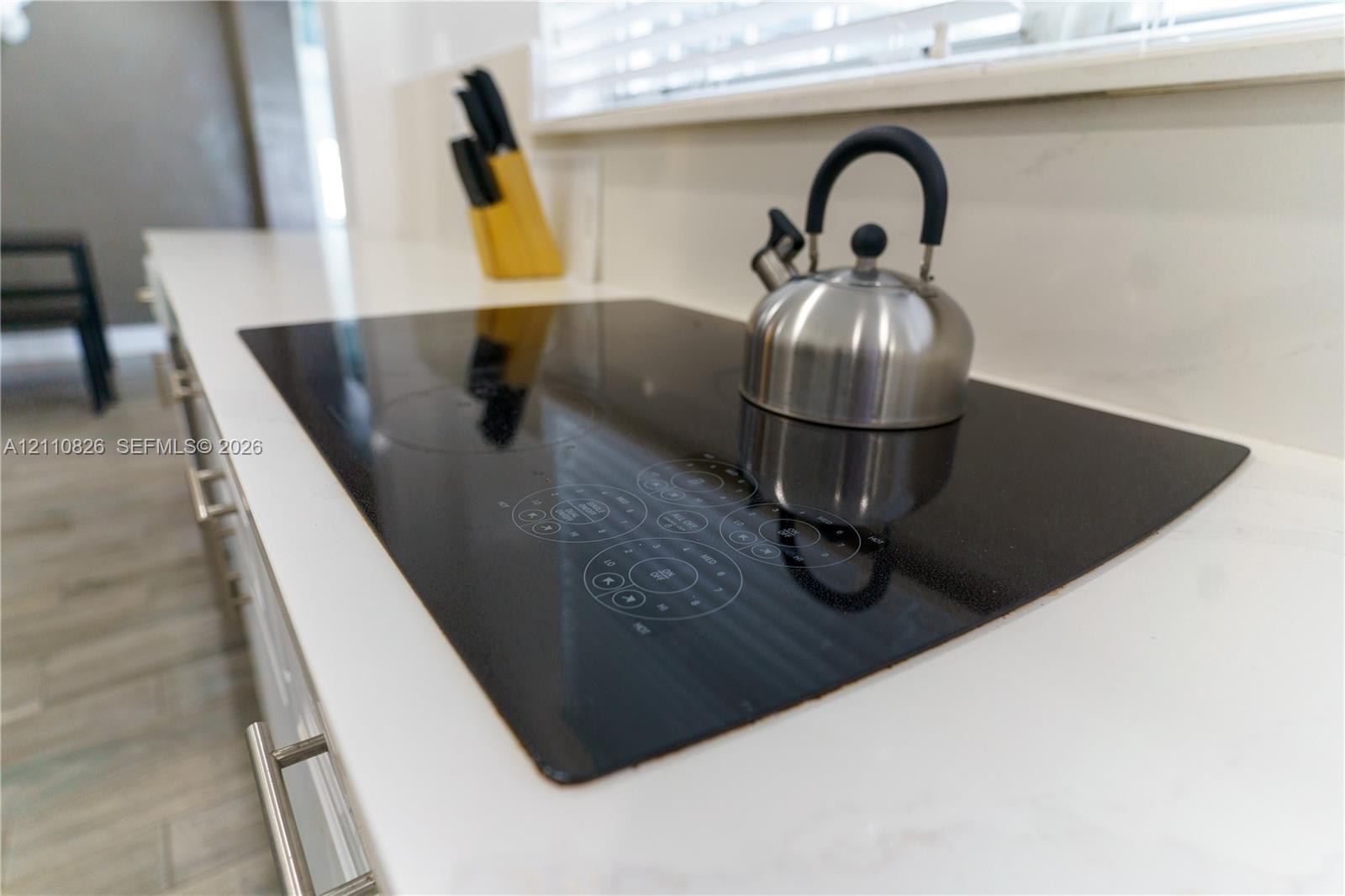 Flush-mount electric cooktop with touch-control interface, integrated into a white countertop with light veining and wood-finish flooring