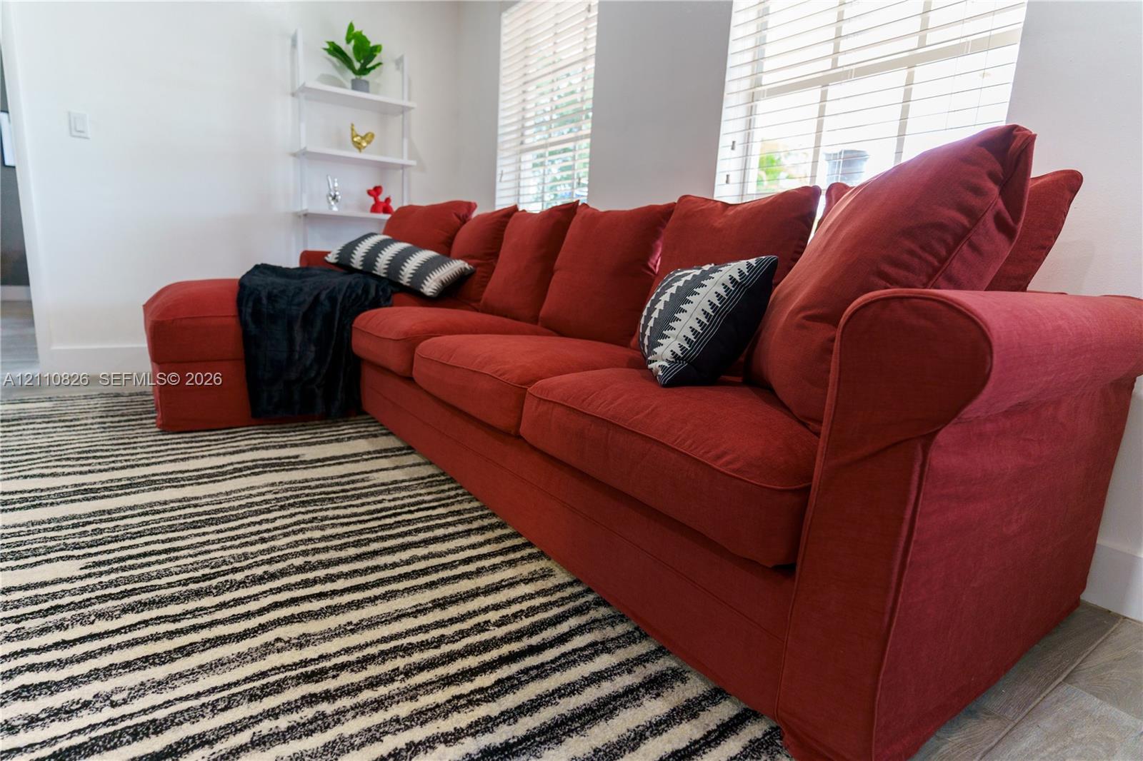 Room featuring neutral-toned walls, wood-finish flooring, and multiple windows fitted with horizontal blinds