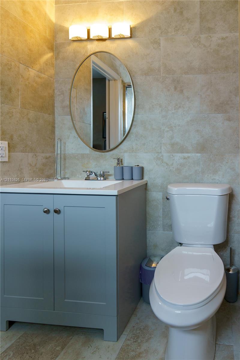 Blue-toned vanity with a rectangular sink, wall-mounted oval mirror, three-light fixture, and stone-tile wall surfacing