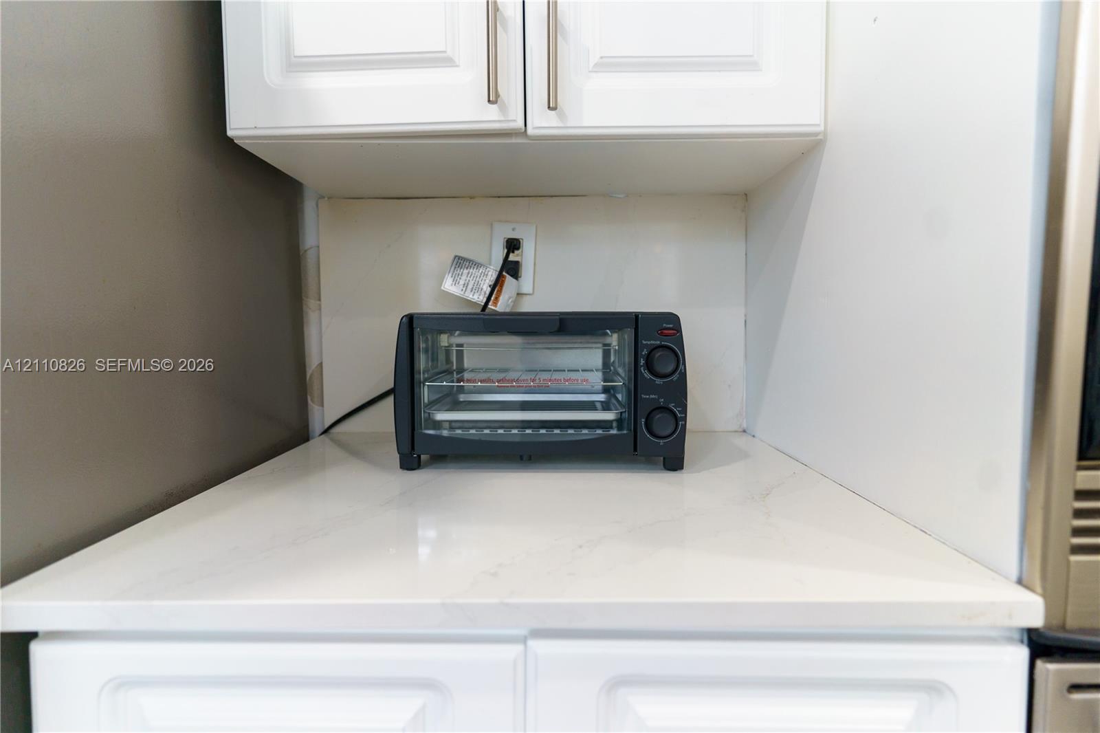 White shaker-style cabinetry with metallic pulls, stone-surface countertop, and smooth-finish backsplash