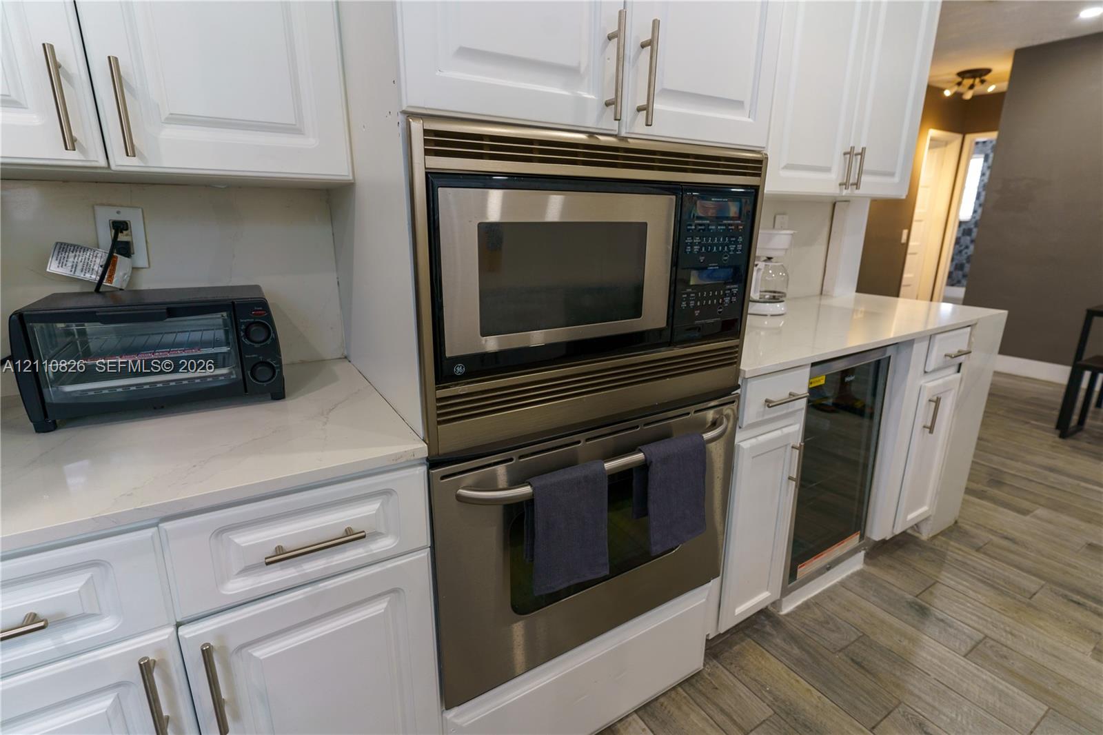 Kitchen featuring white Shaker-style cabinetry, quartz countertops, a built-in stainless steel microwave and oven combination, a stainless steel under-counter beverage cooler, and wood-finish flooring