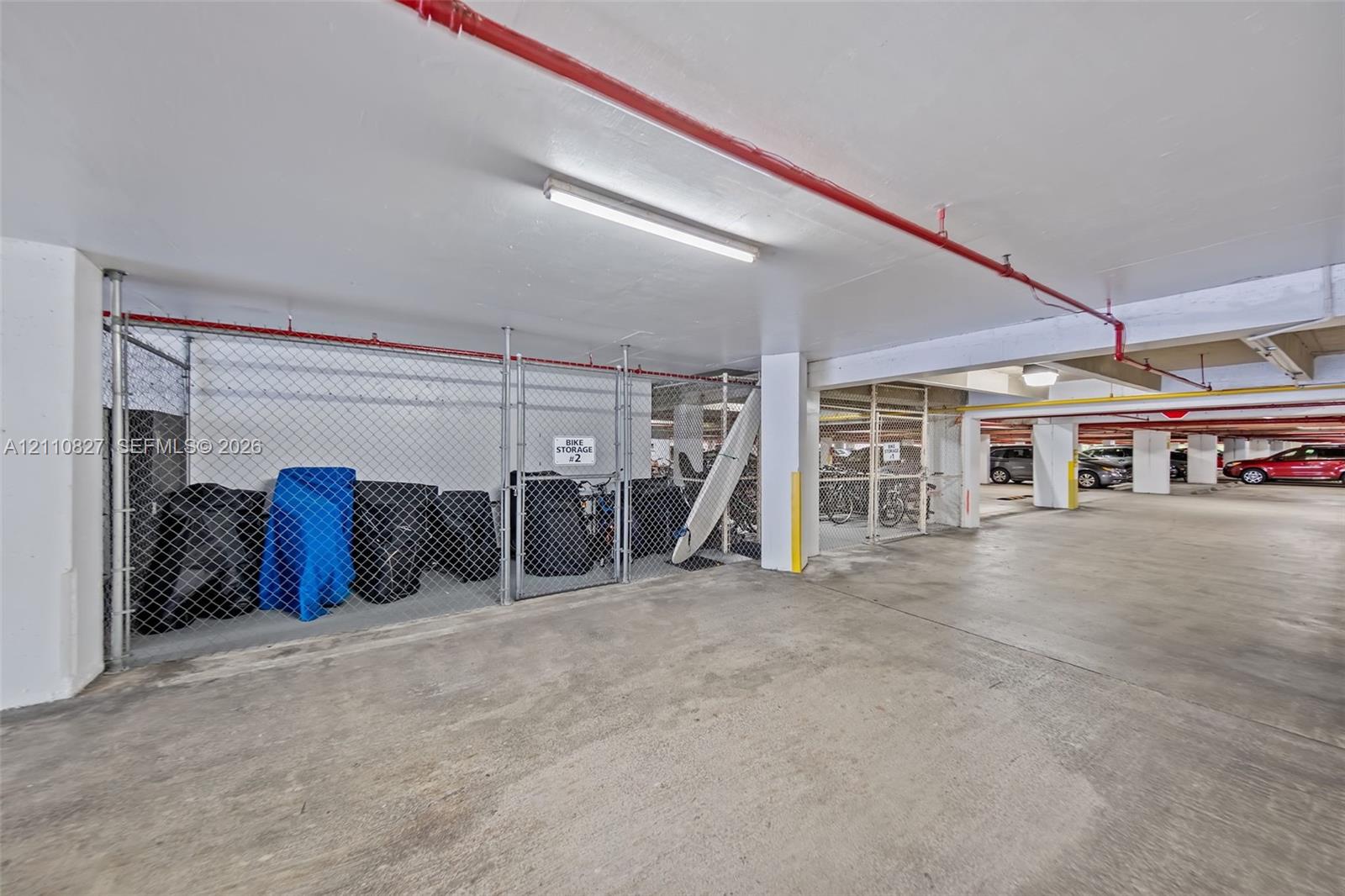 Covered parking area featuring concrete flooring, chain-link storage lockers, and overhead lighting