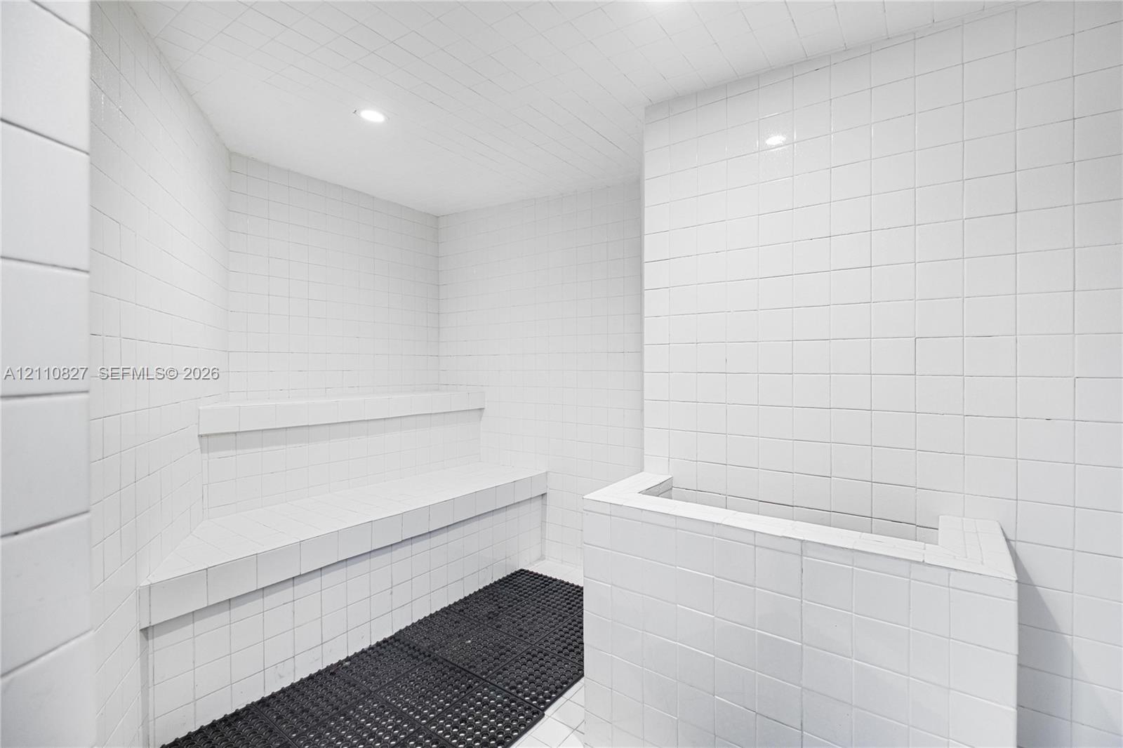 Steam room featuring white square wall tile, recessed ceiling lighting, and a built-in tiled bench