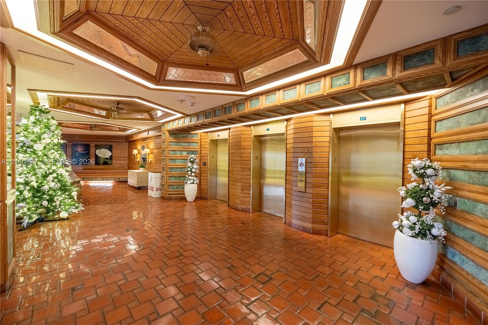 Lobby entrance featuring hexagonal wood-paneled ceilings with recessed accent lighting, metallic-finish elevator doors, and horizontal wood wall paneling with inset tile detailing over terracotta flooring