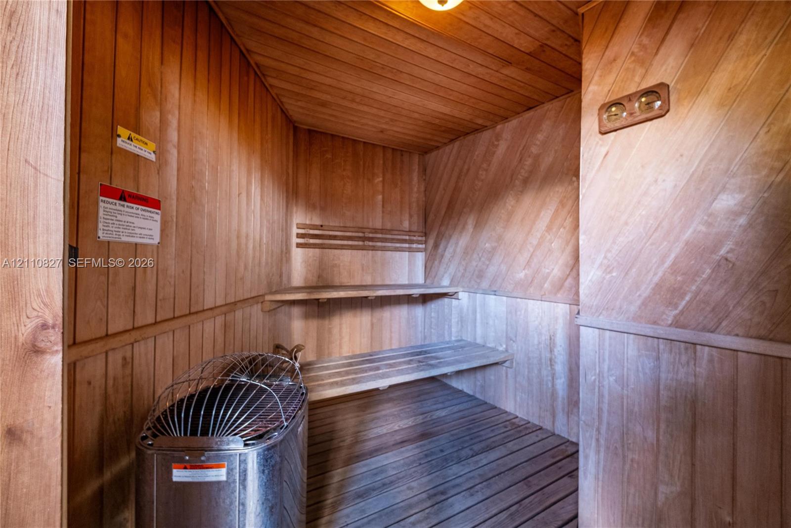 Sauna interior featuring natural wood-paneled walls, built-in tiered wooden benches, slatted wood flooring, and a metal sauna heater with a protective cage