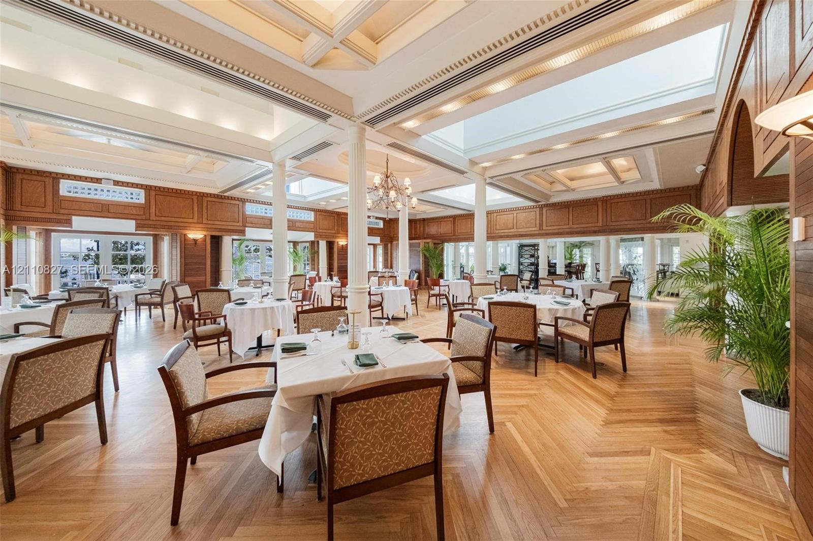 Expansive interior space featuring coffered ceilings, skylights, intricate wall paneling, structural columns, and herringbone-pattern wood-finish flooring