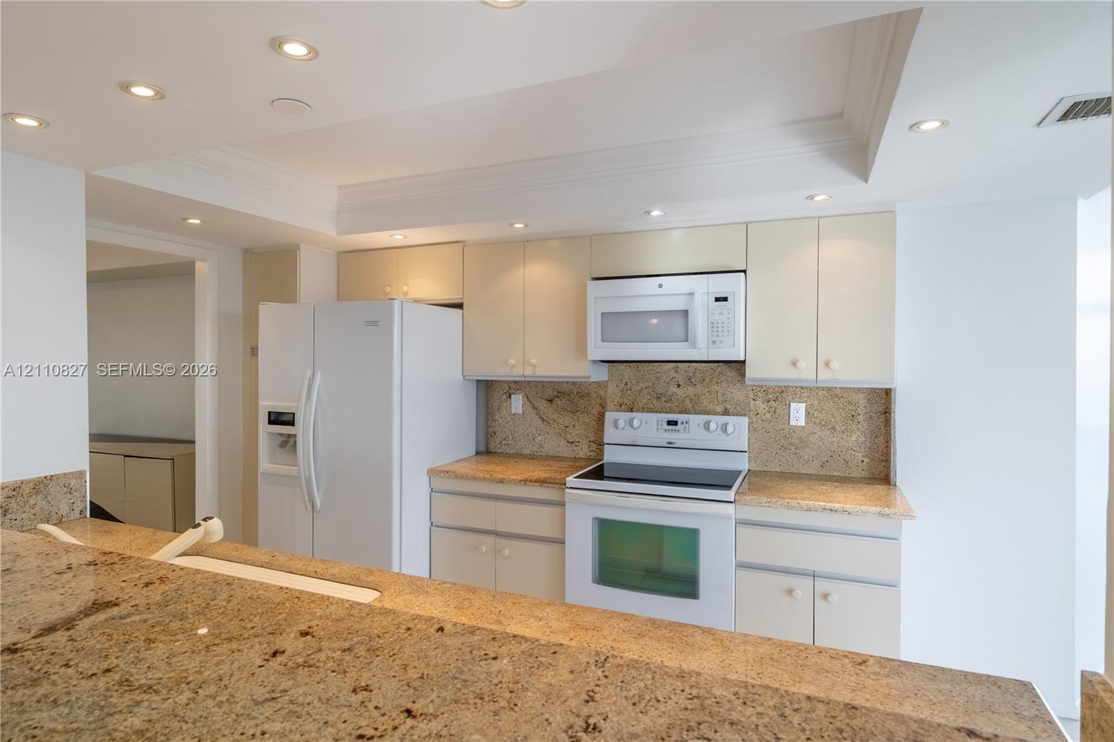 Kitchen featuring stone countertops, integrated cabinetry, white appliances, and recessed ceiling lighting