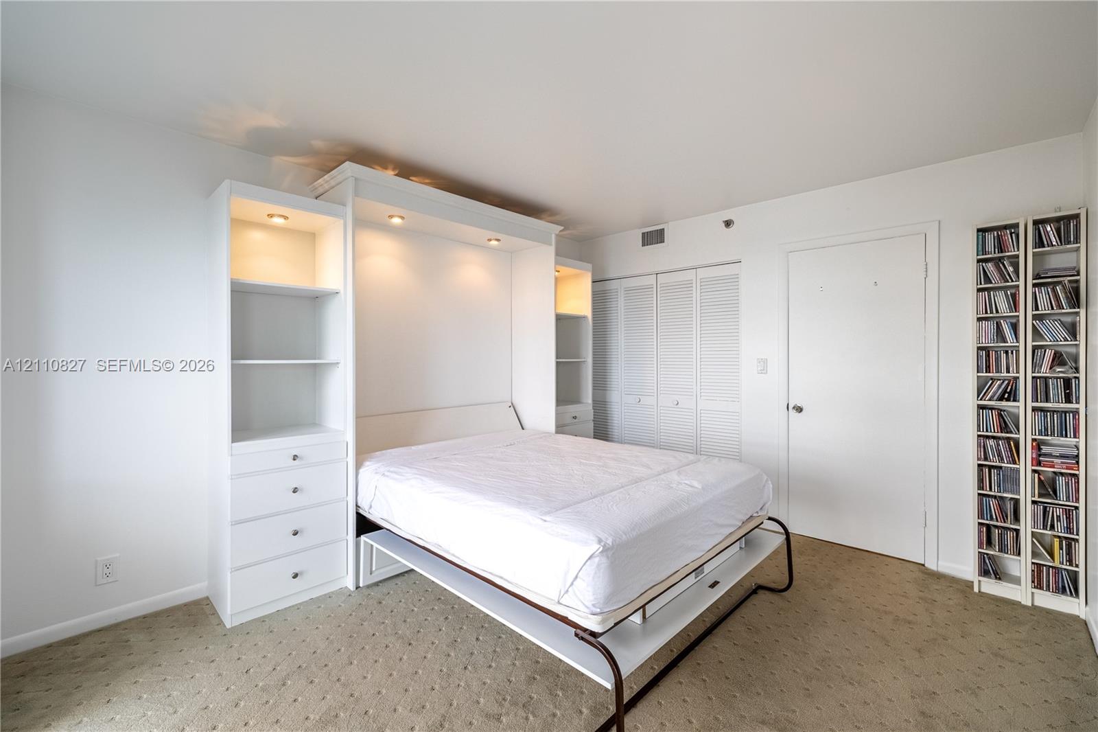 Custom white built-in cabinetry featuring integrated recessed lighting, four drawers, and shelving, paired with white louvered closet doors and carpeted flooring