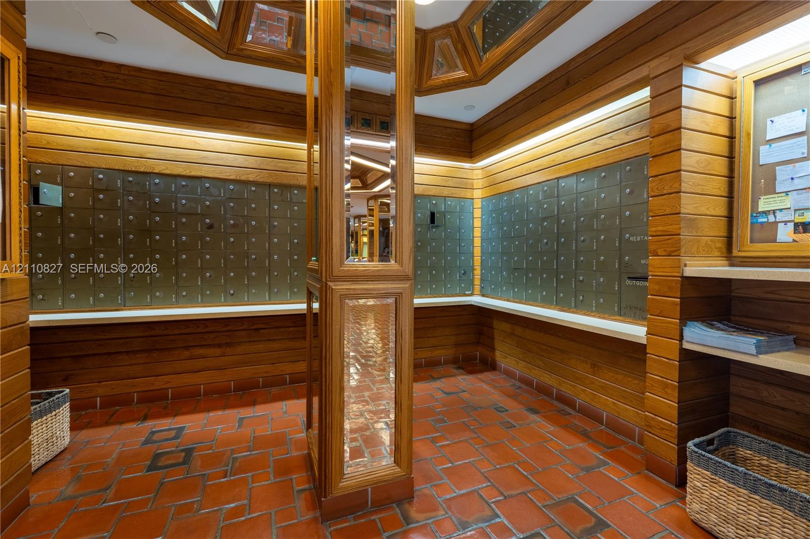 Mailroom area featuring horizontal wood paneling, terracotta tile flooring, built-in metal mailboxes, integrated task lighting, and a central column with mirrored accents