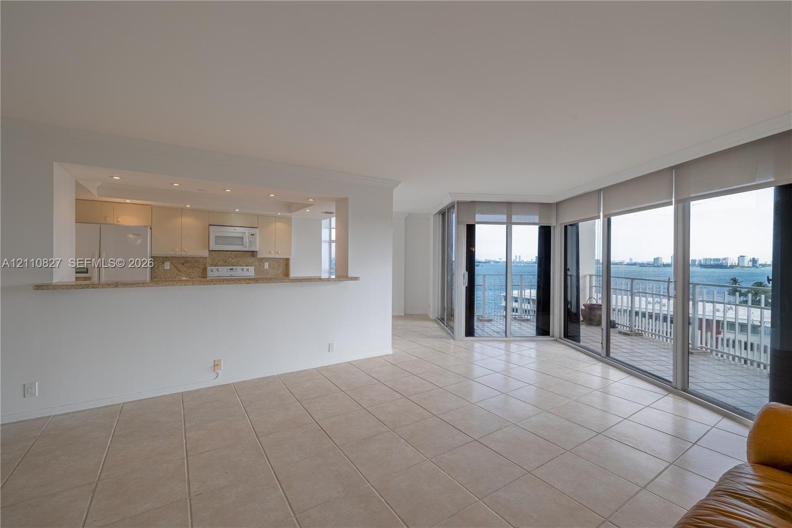 Open-concept living space with tile flooring, pass-through kitchen counter, recessed lighting, and expansive floor-to-ceiling glass sliding doors leading to a balcony