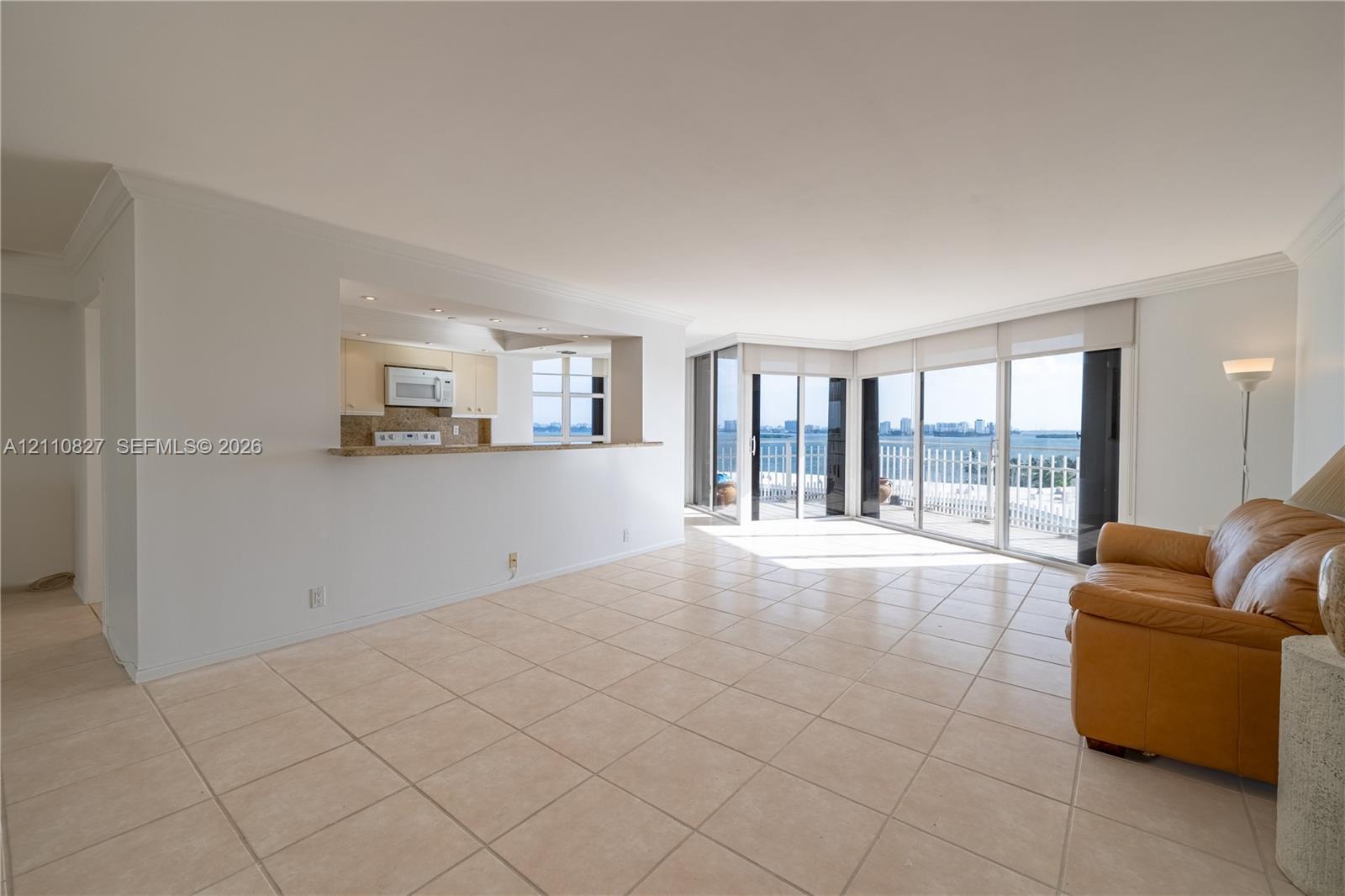 Open-concept area featuring light-toned ceramic tile flooring, a pass-through kitchen counter, and floor-to-ceiling glass sliding doors leading to an exterior balcony