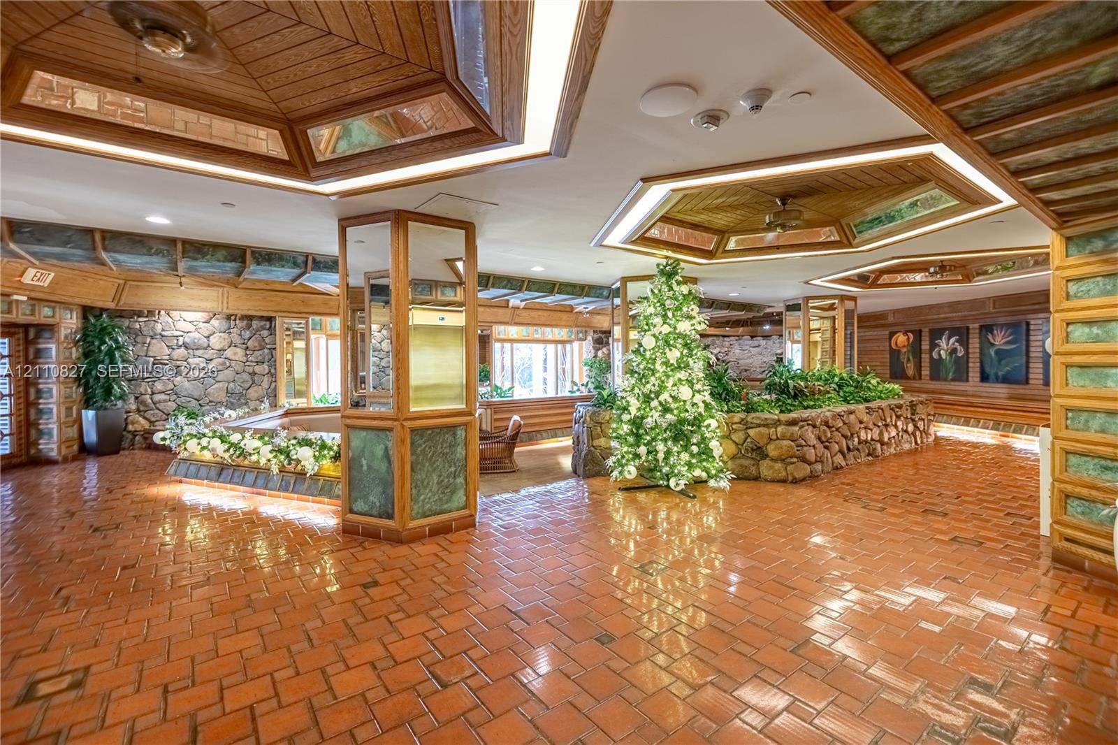 Spacious interior featuring terra-cotta tile flooring, wood-paneled tray ceilings with integrated lighting, custom stone accent walls, and mirrored support columns