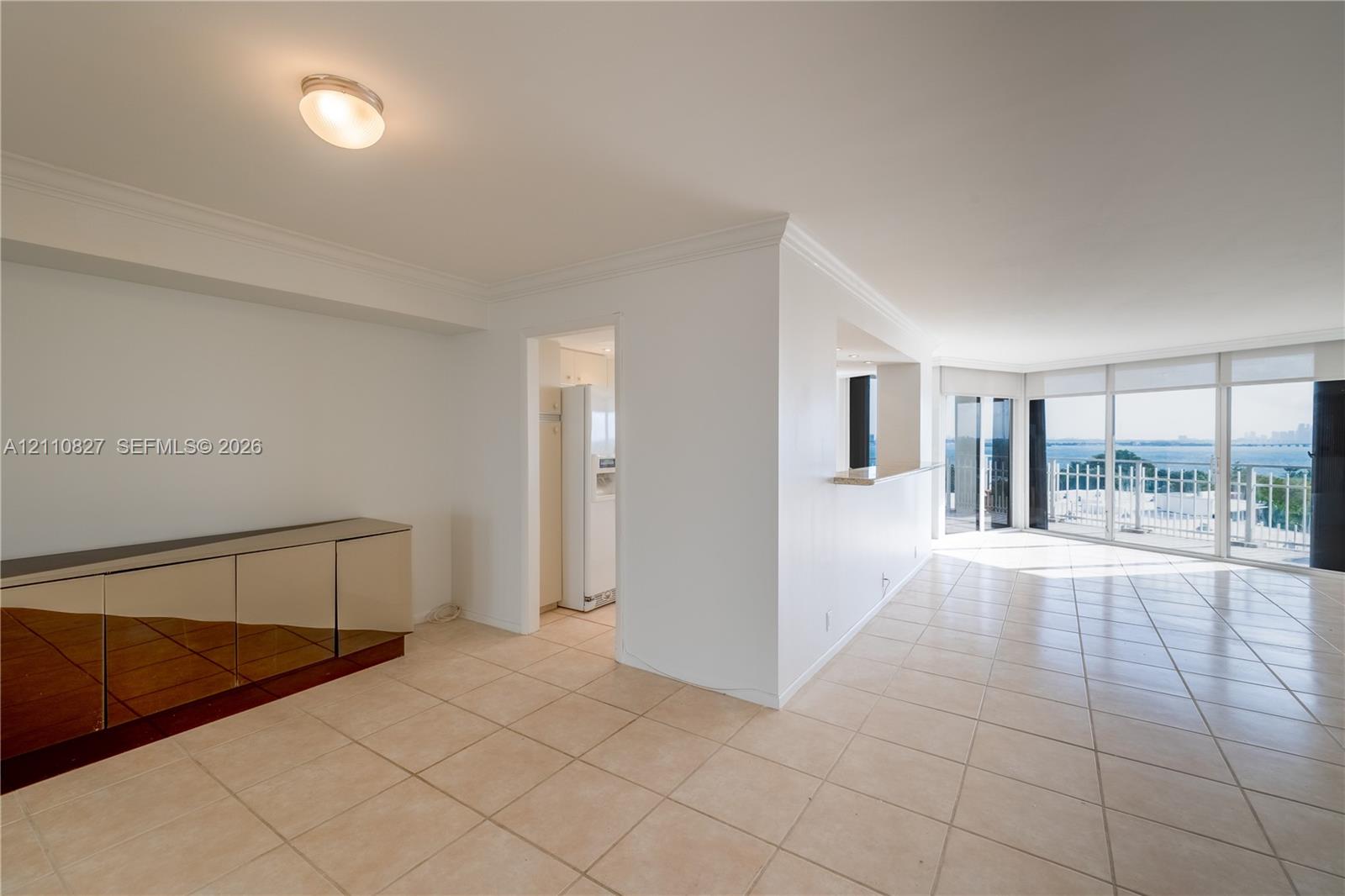 Open floor plan featuring light-toned tile flooring, built-in mirrored cabinetry, a pass-through counter, and floor-to-ceiling windows