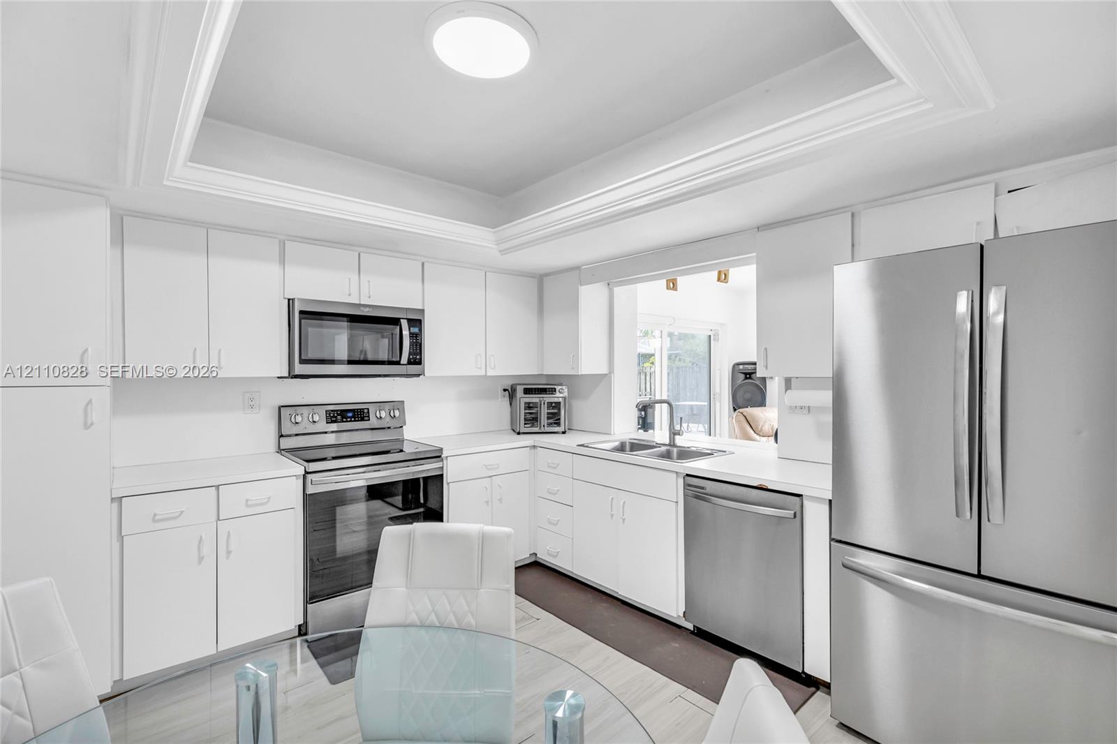 Kitchen featuring white shaker-style cabinetry, stainless steel appliances, a tray ceiling, and a dual-basin undermount sink with a gooseneck faucet