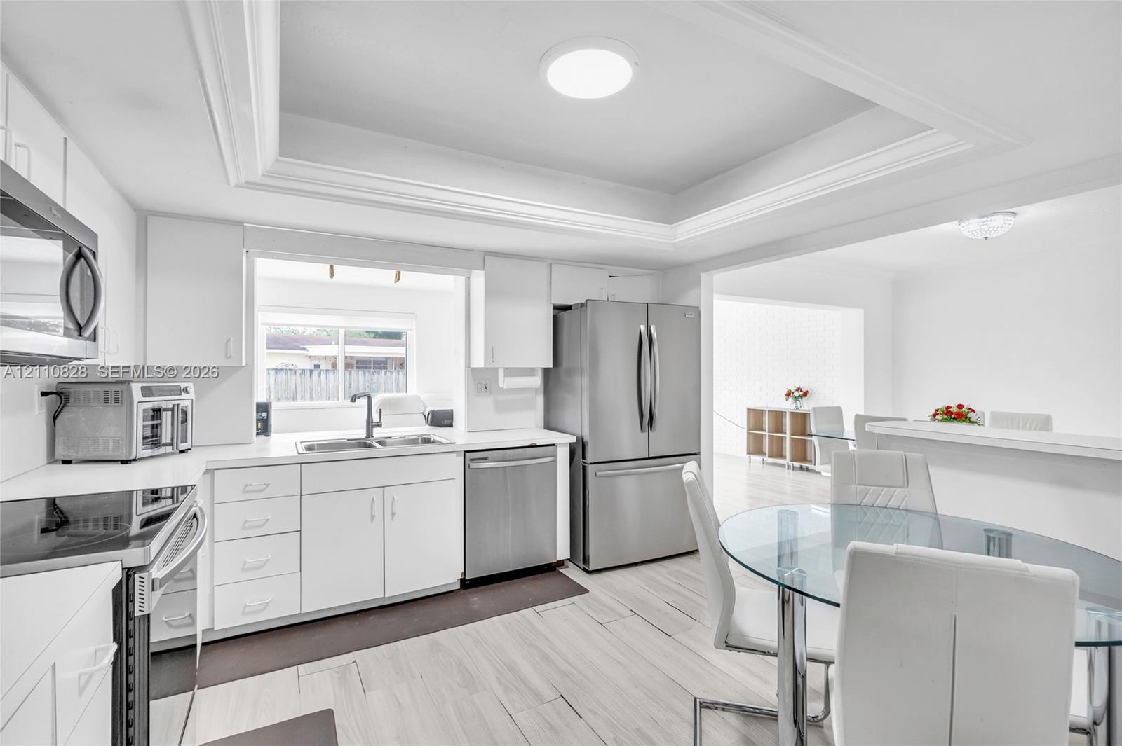 Kitchen featuring white cabinetry, stainless steel appliances, wood-finish flooring, and a tray ceiling