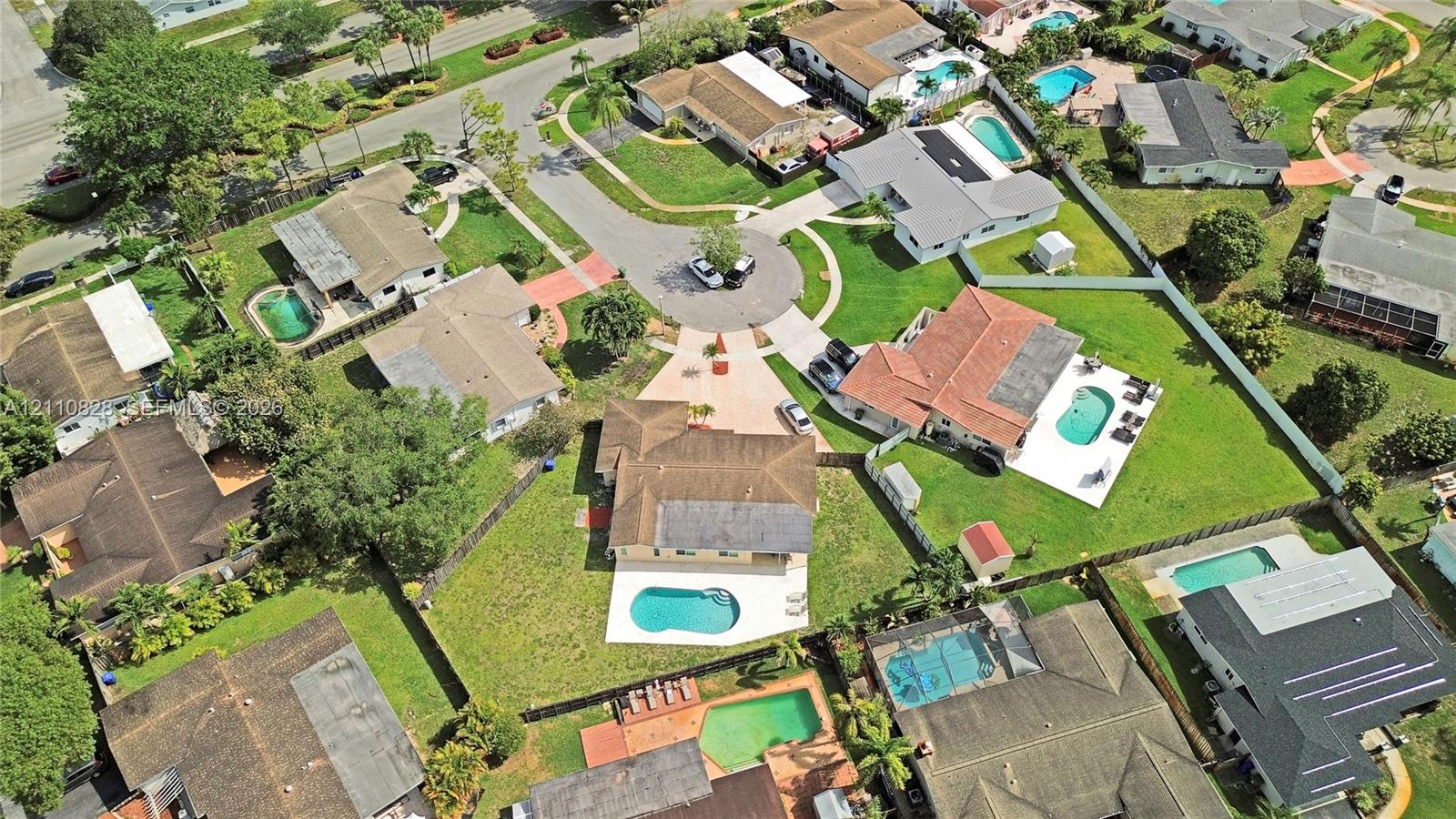 Aerial view of a residential property featuring an in-ground swimming pool, a concrete patio, and a manicured lawn