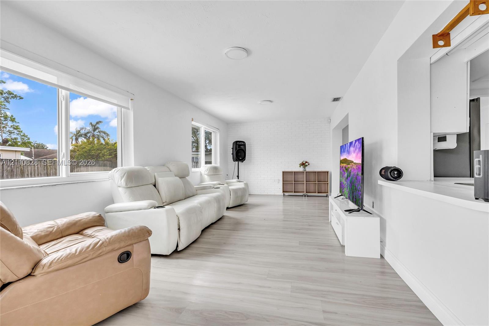 Interior living space featuring wood-finish flooring, a white painted brick accent wall, and expansive windows