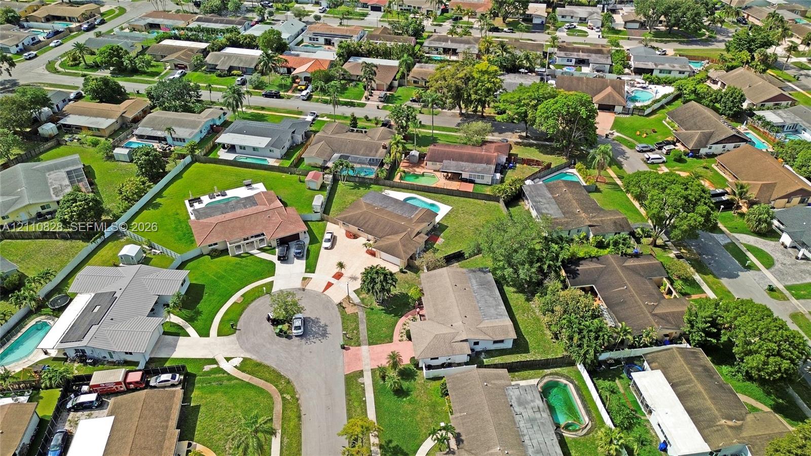 Aerial perspective of a suburban neighborhood characterized by varied residential architectural styles, intersecting paved streets, established mature tree canopy, and green spaces