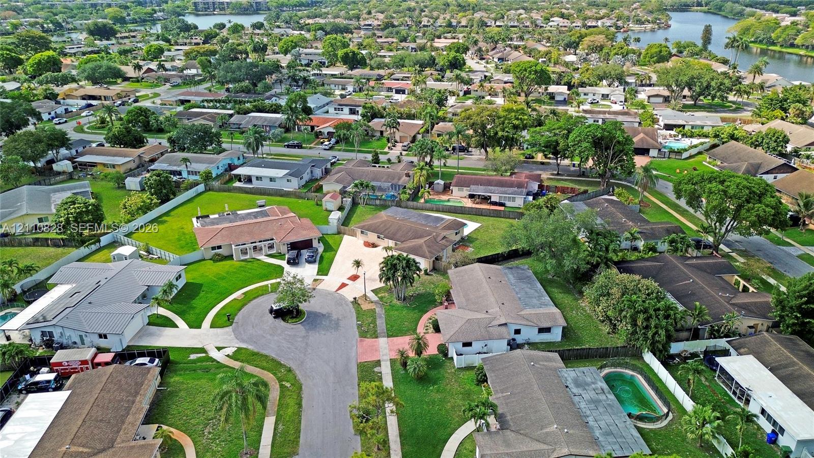 Aerial perspective of a suburban neighborhood featuring a cul-de-sac, winding roadways, mature trees, manicured lawns, and proximity to a waterway