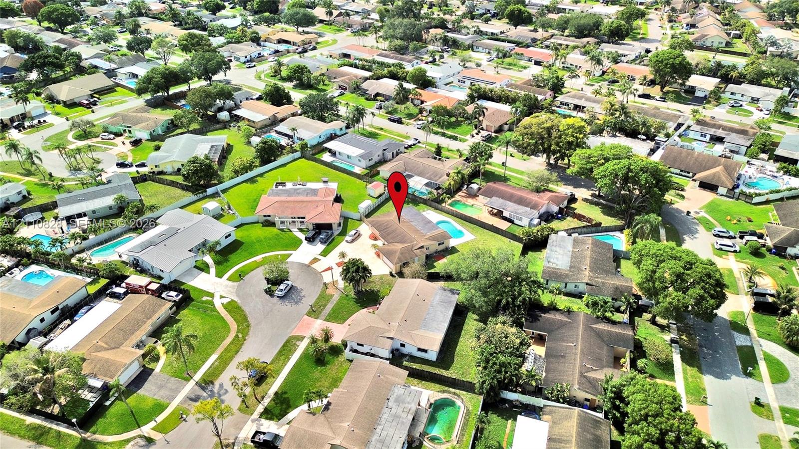 Aerial perspective of a suburban neighborhood featuring residential lots with mature trees, established landscaping, paved roadways, and private swimming pools