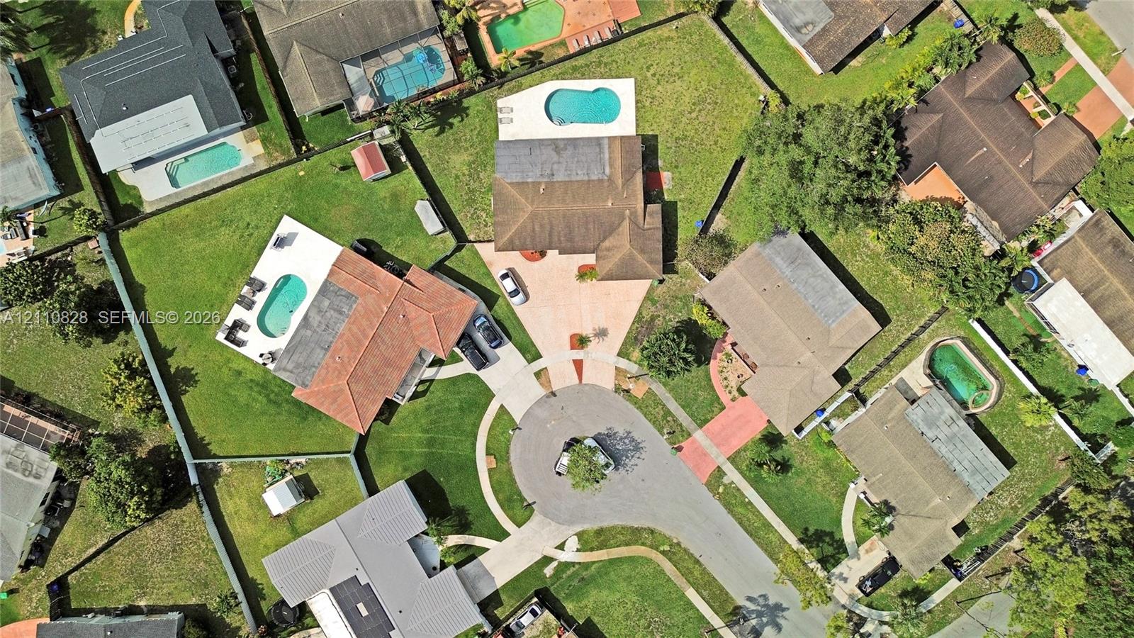 Aerial perspective of the property featuring a rectangular in-ground swimming pool, concrete paved driveway, shingle roofing, and established lawn area
