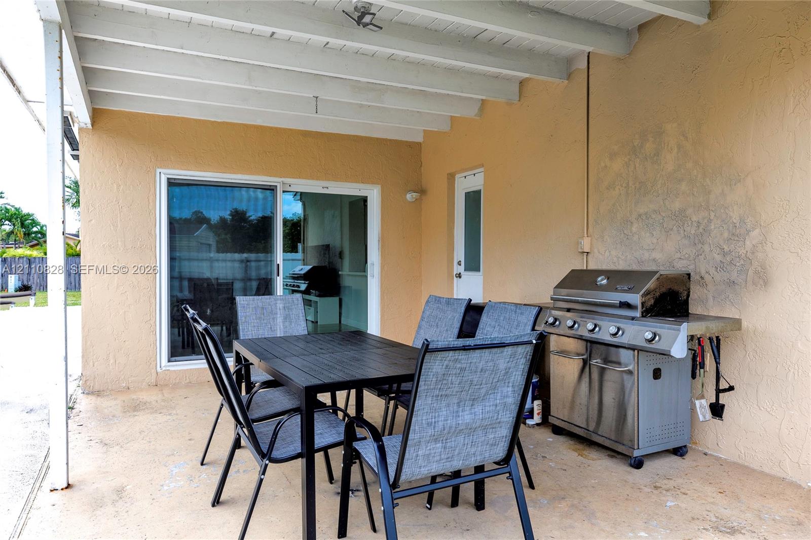 Covered patio featuring a concrete floor, exposed ceiling joists, sliding glass door, and a built-in metal outdoor grill