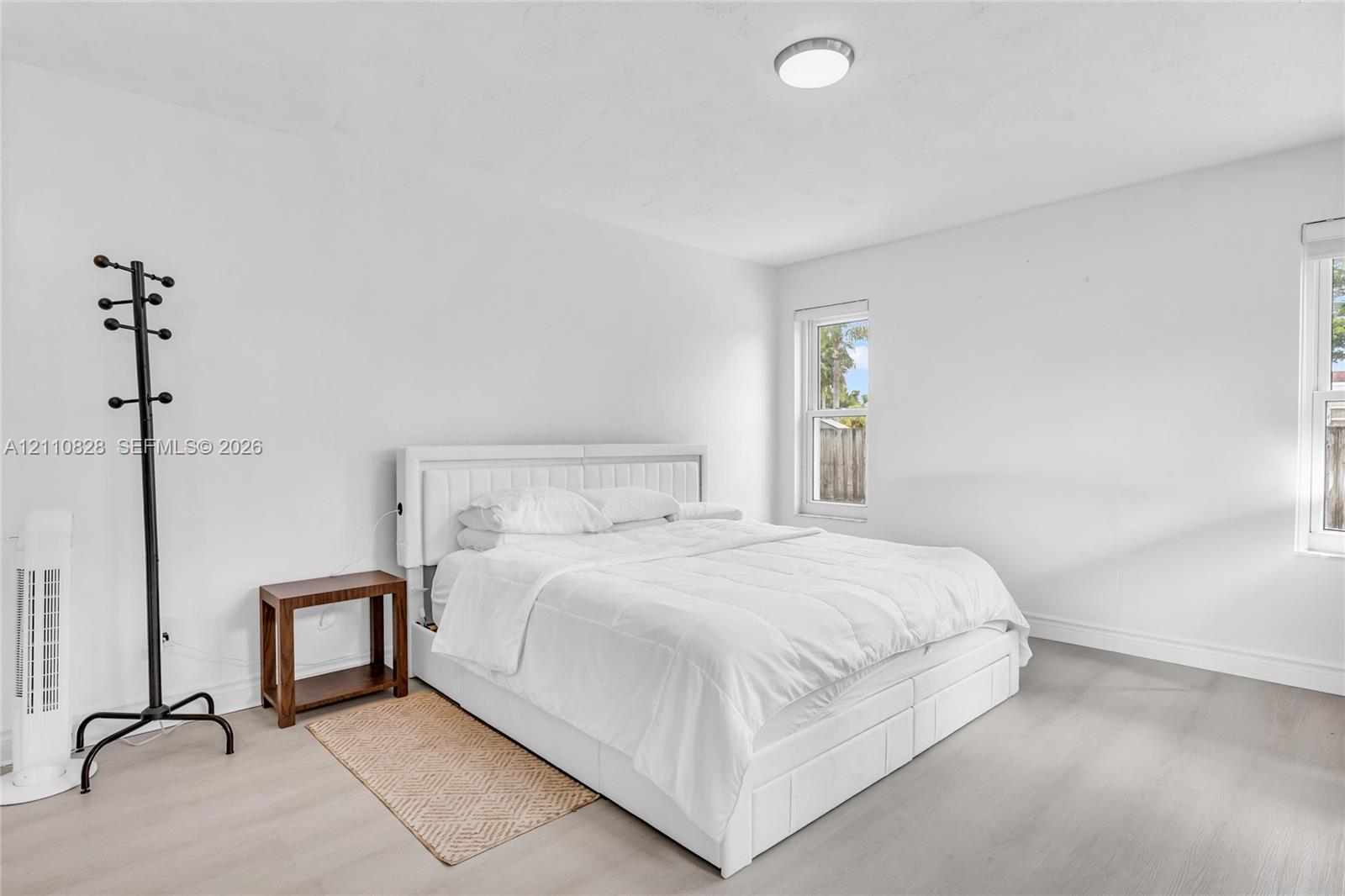 Neutral-toned wood-finish flooring, two double-pane windows, and a flush-mount ceiling light fixture
