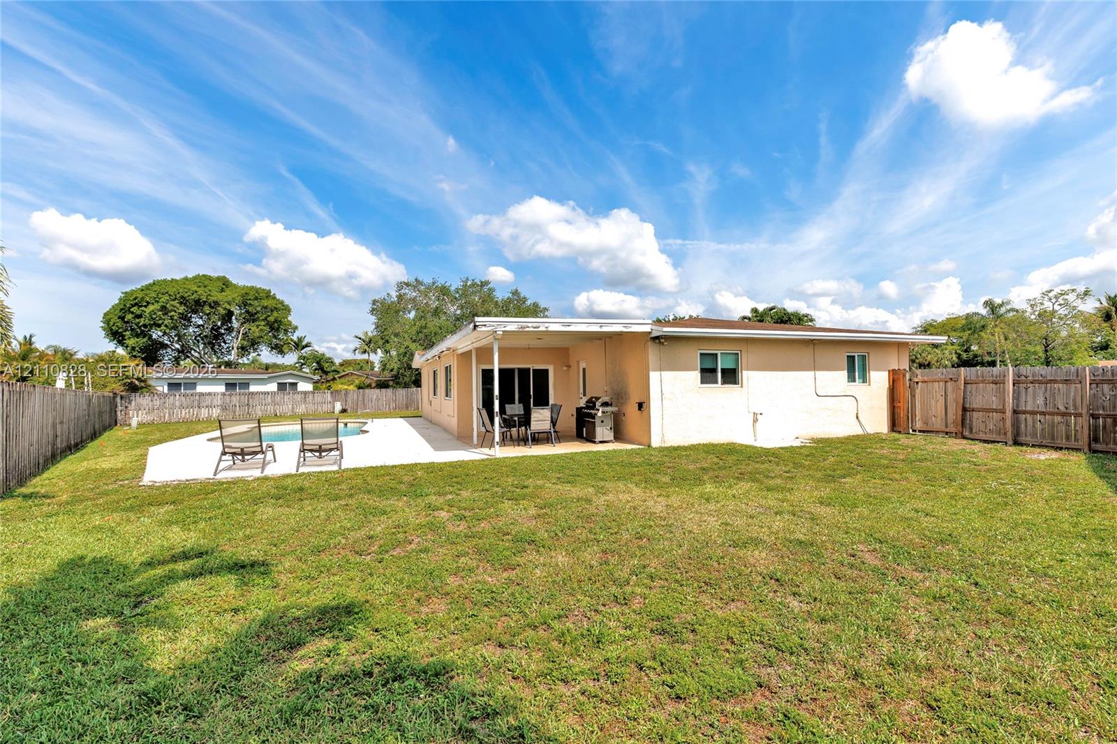Rear exterior featuring a covered patio, concrete pool deck, in-ground pool, and wood privacy fencing surrounding the grass lawn