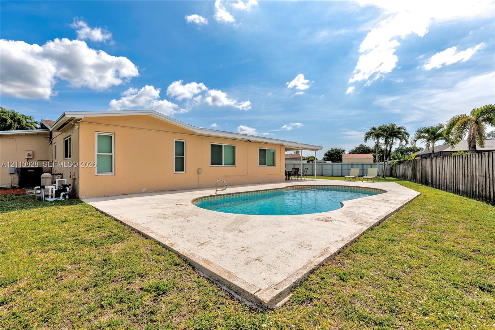 In-ground swimming pool with a concrete patio, stucco exterior siding, and perimeter wood fencing