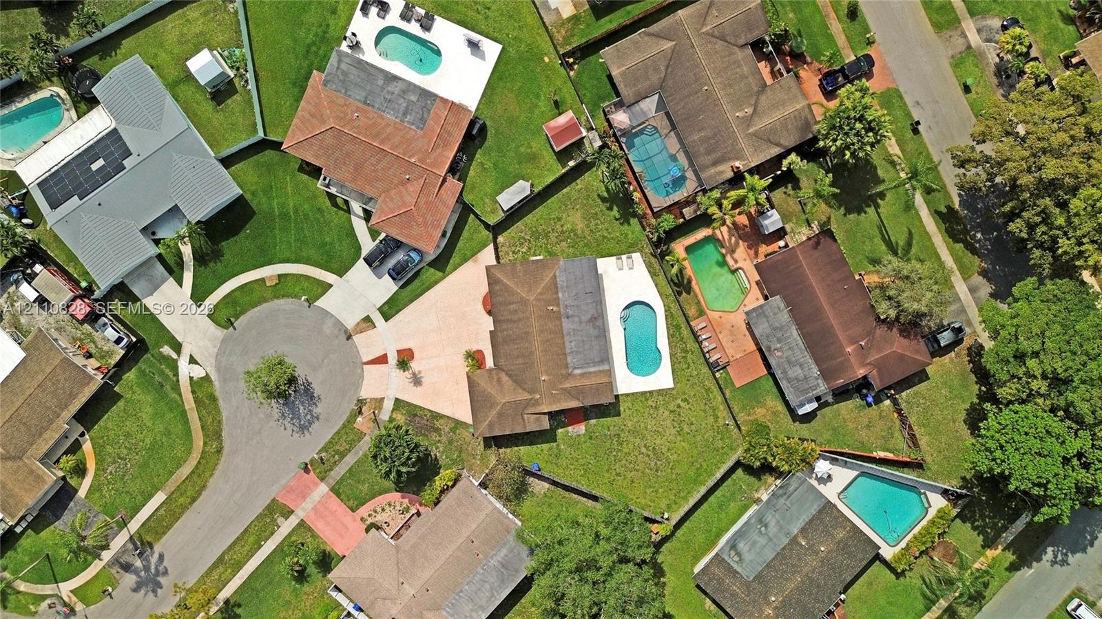 Aerial perspective of a cul-de-sac residential property featuring a multi-hipped roofline, private swimming pool, concrete patio, and established lawn