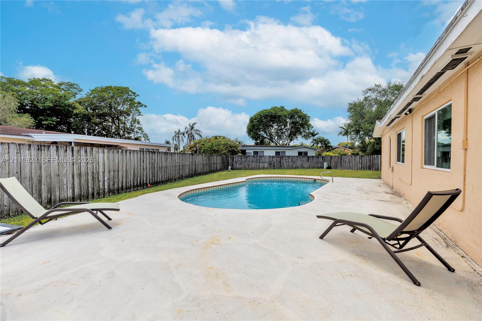 Backyard featuring an in-ground swimming pool, concrete patio, perimeter wood fencing, and a grass lawn