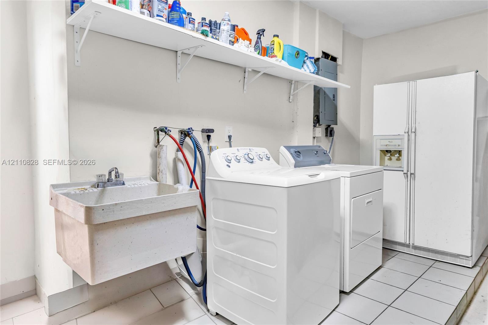 Utility space featuring tile flooring, a wall-mounted utility sink with metal faucet, and built-in open shelving