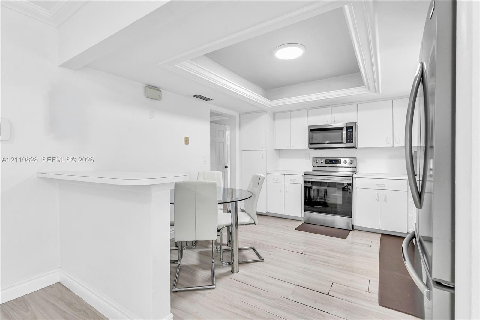 Kitchen featuring white cabinetry, stainless steel appliances, tray ceiling, and wood-finish flooring with a peninsula counter