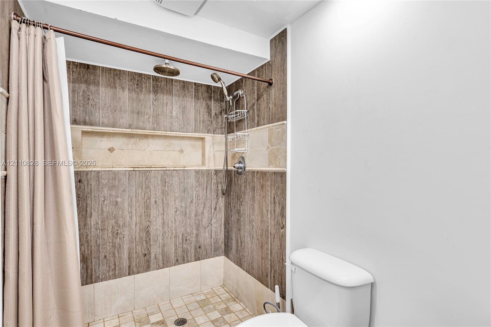 Shower featuring wood-finish wall tile, integrated tile recessed shelving, stone-composite floor tile, and a multi-function shower head system