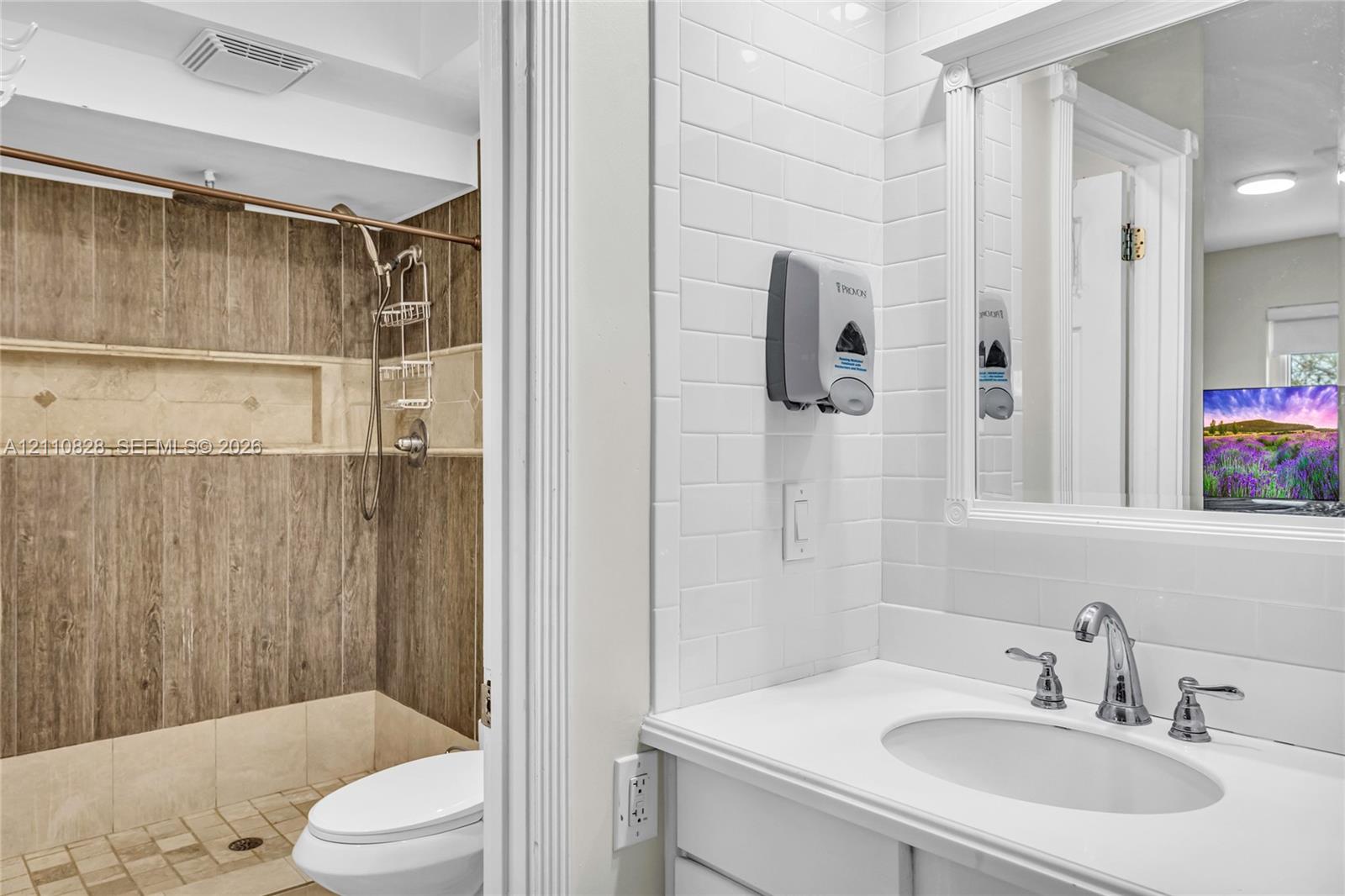 Bathroom featuring white subway tile walls, a vanity with an integrated basin, a framed mirror, and a walk-in shower with wood-finish wall paneling and a recessed niche