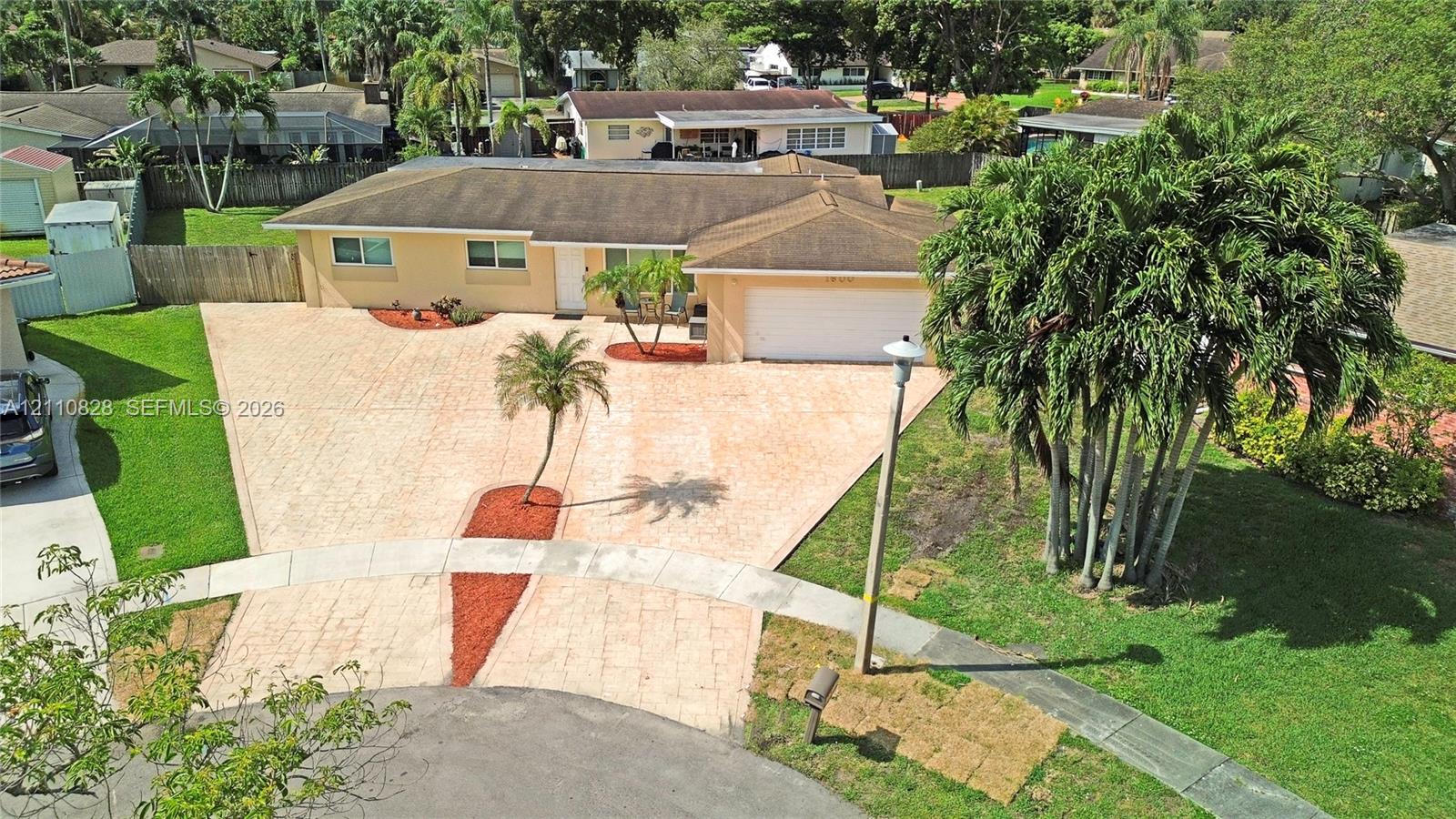 Single-story residence featuring a paver driveway, attached garage, manicured lawn, and mature palm landscaping